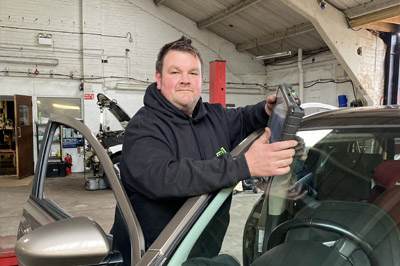 Smiling KCS mechanic with a diagnostic tool at a car door