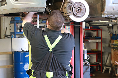 Mechanic working on a brake disc under a raised car